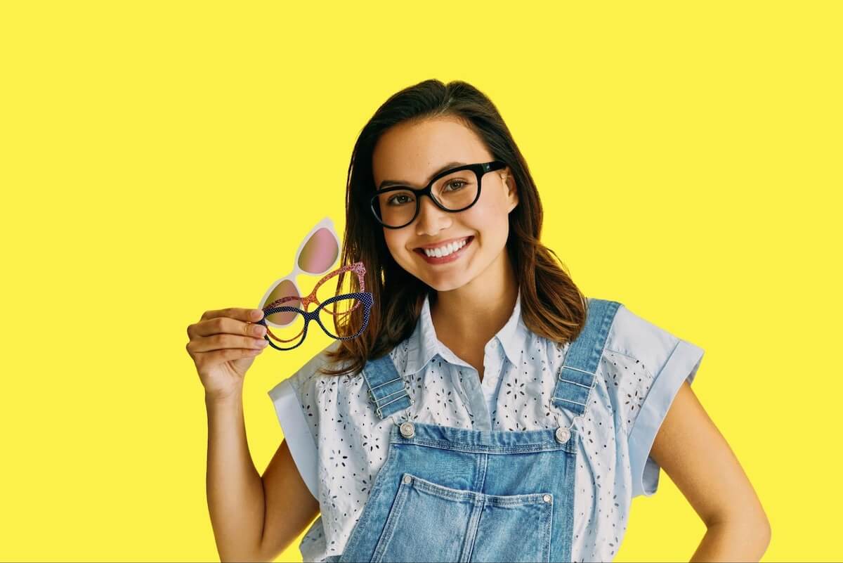 How often should you get new glasses: woman holding 3 pairs of eyeglasses while smiling at the camera